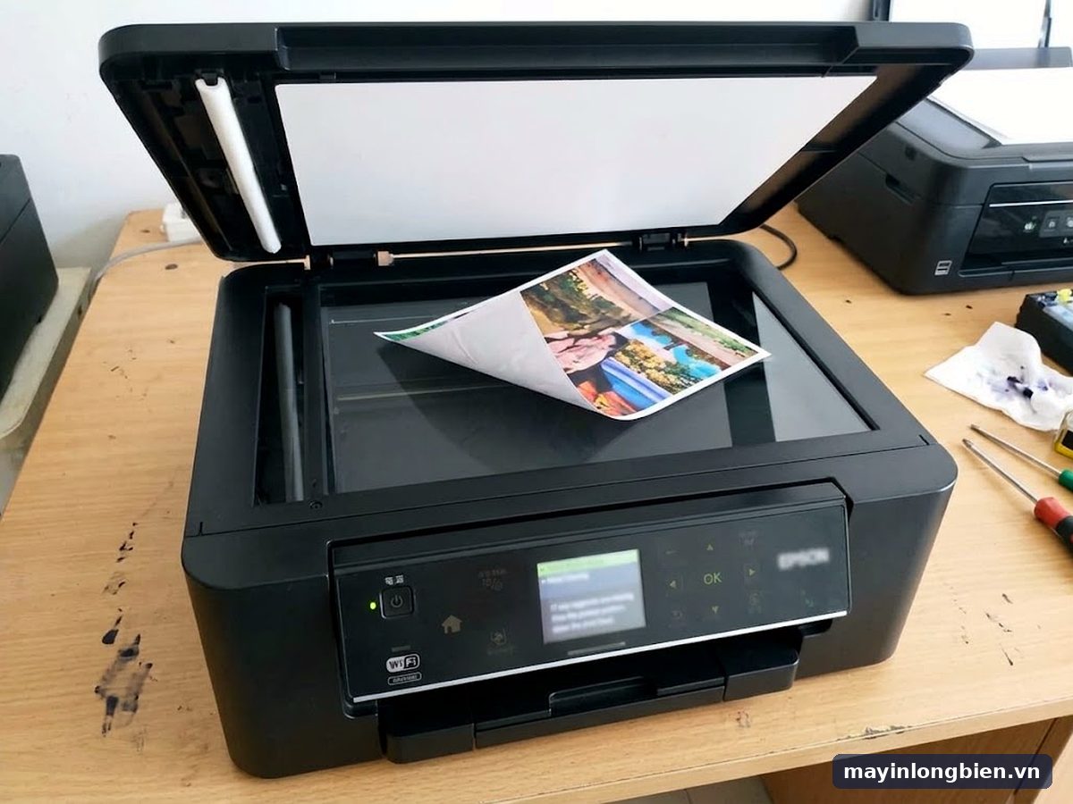Máy in đa năng màu đen có nắp scan mở, tờ ảnh đặt trên mặt kính scan